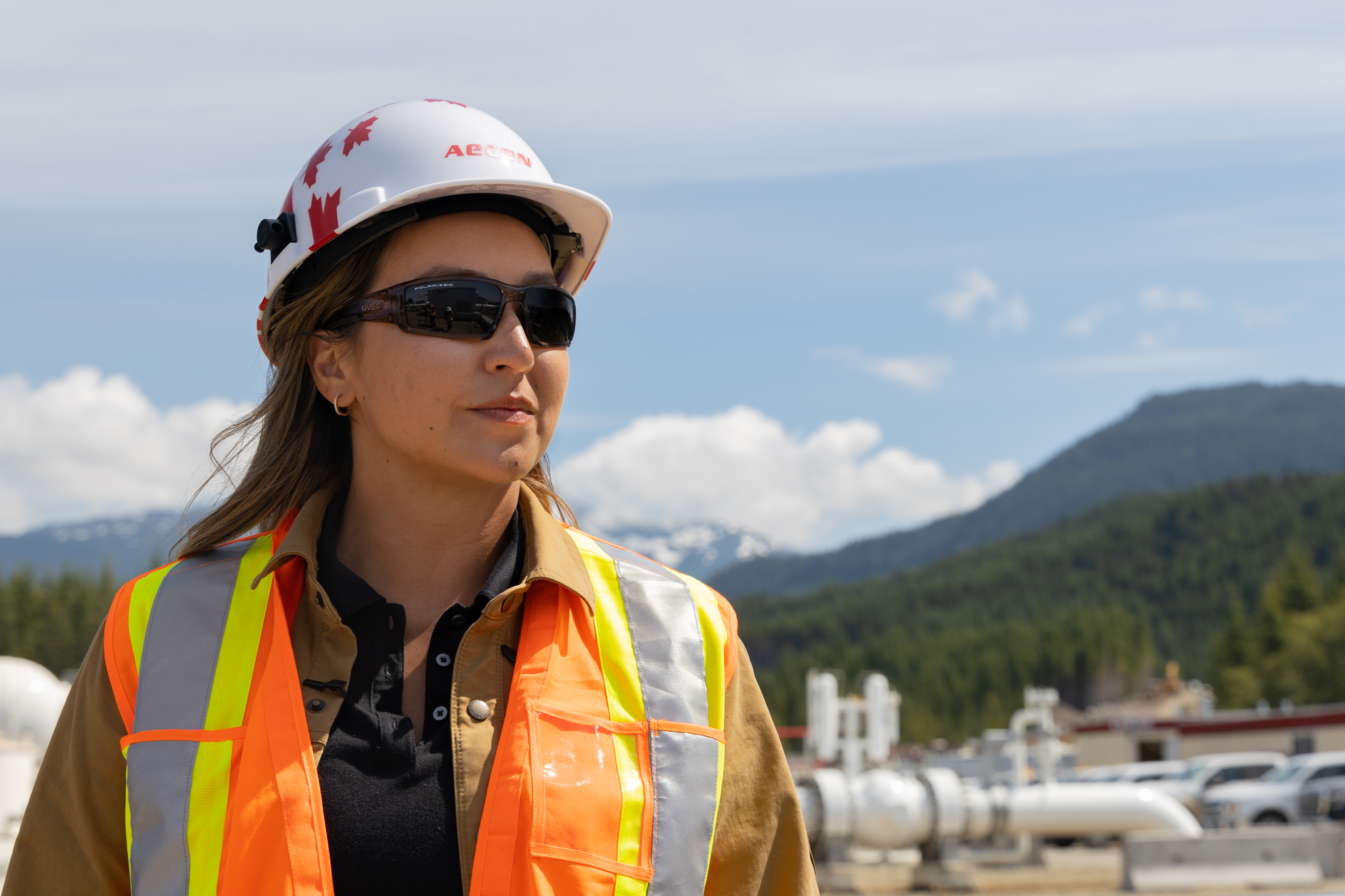 Woman in construction hat looking off into the distance with mountains in the background