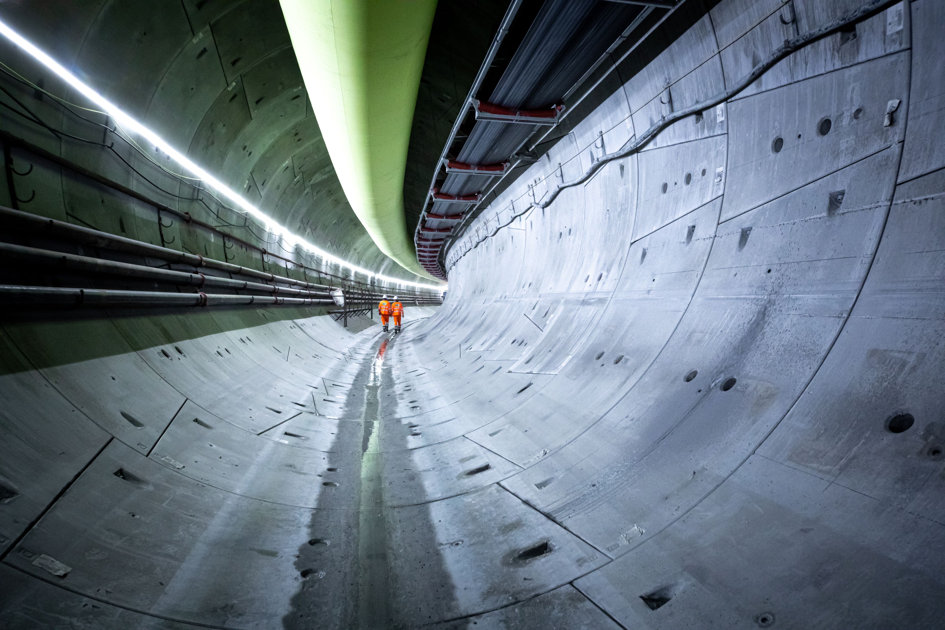 A completed tunnel, with no tracks and systems installed. There is two people in full high visibility gear.